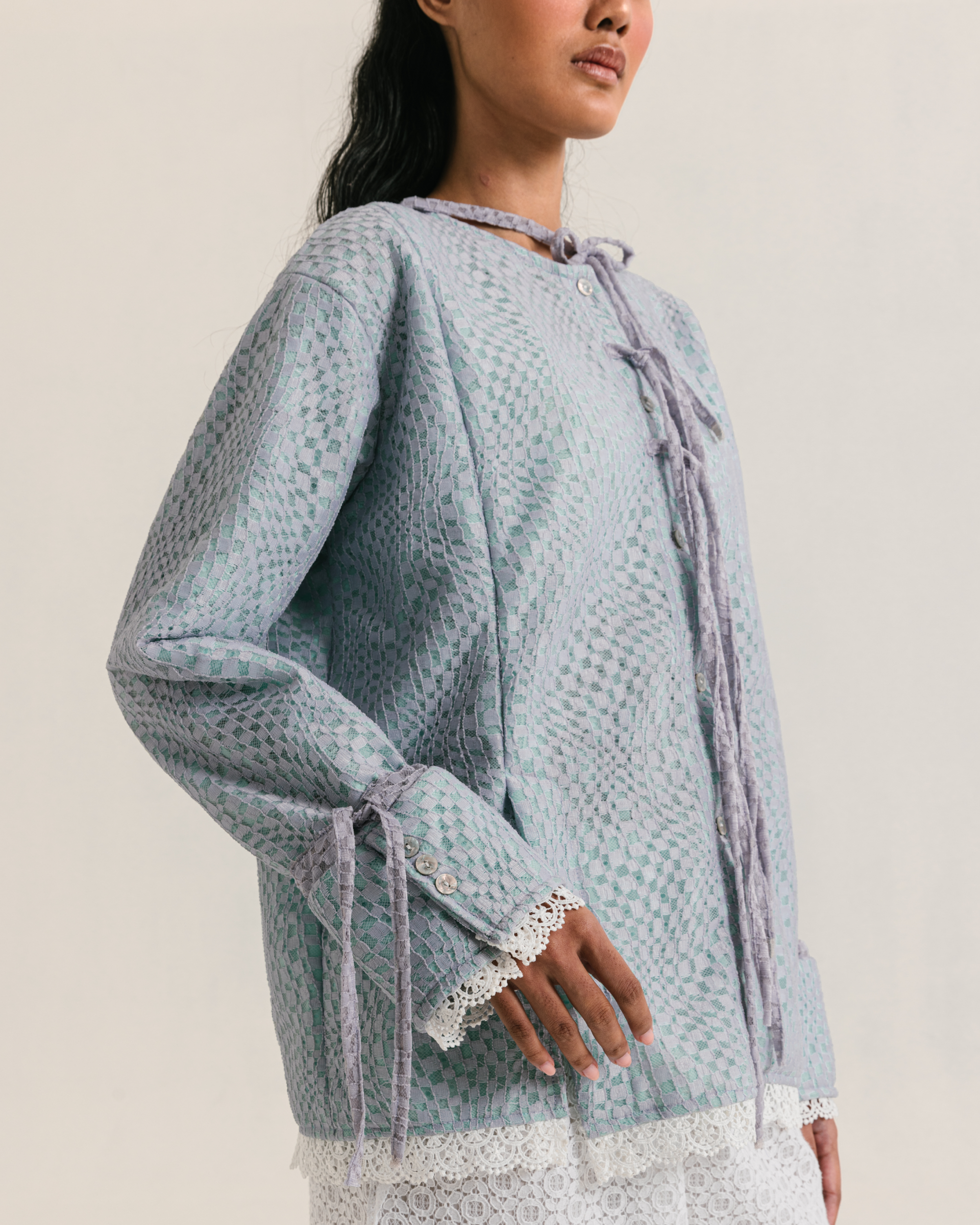 Image of Lottie Lace Blouse, a loose-fitting blouse made from brocade with cotton lining underneath, adorned with ties detailing on the front up to the neckline.